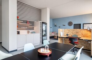 A modern office space with a conference table, white chairs, a kitchen area, and a blue wall with decorative items. - ipartment Braunschweig @HOME by Best Western (Braunschweig)