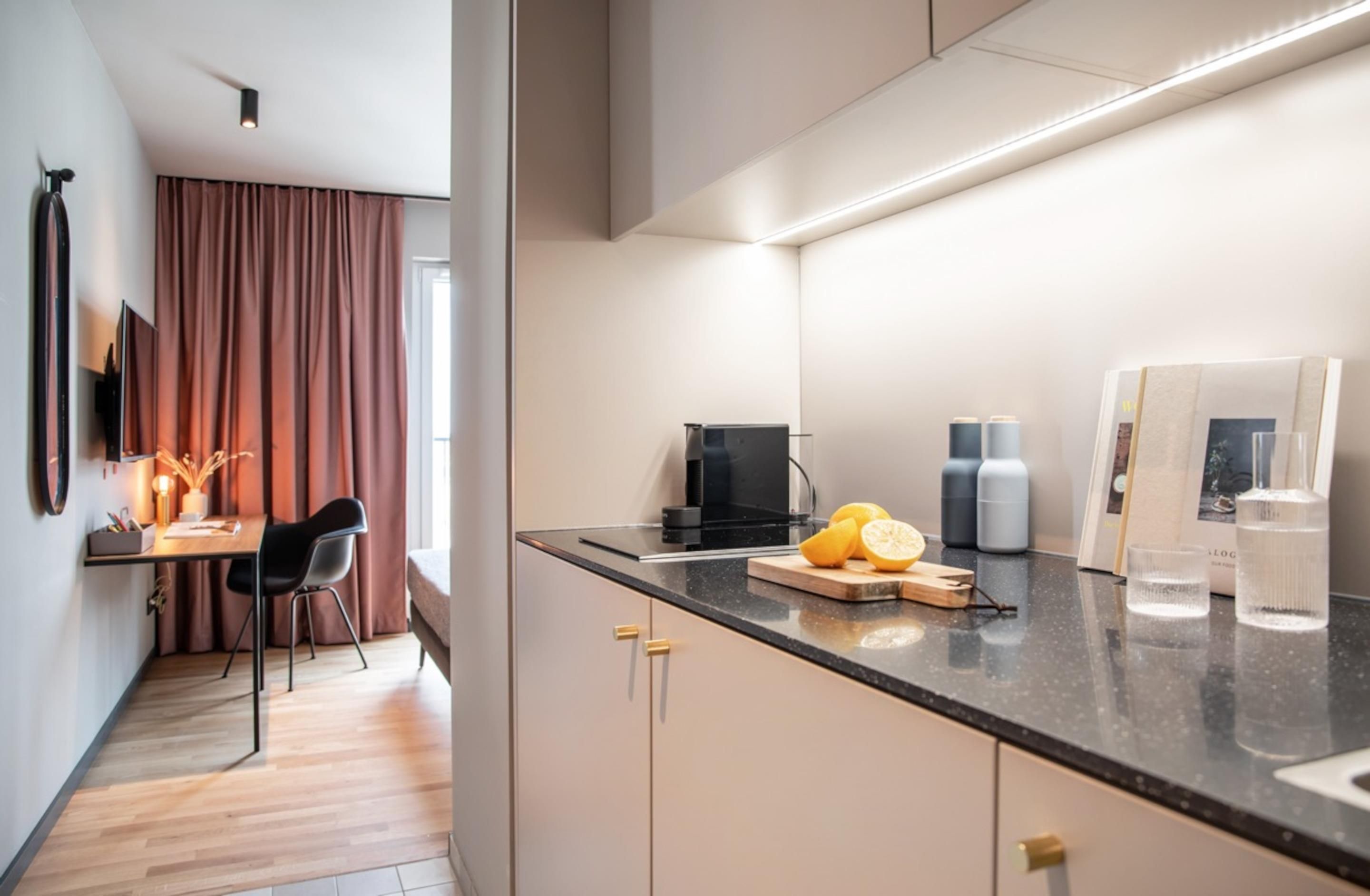 Una cocina moderna con encimera negra, cafetera y tabla de cortar con fruta.