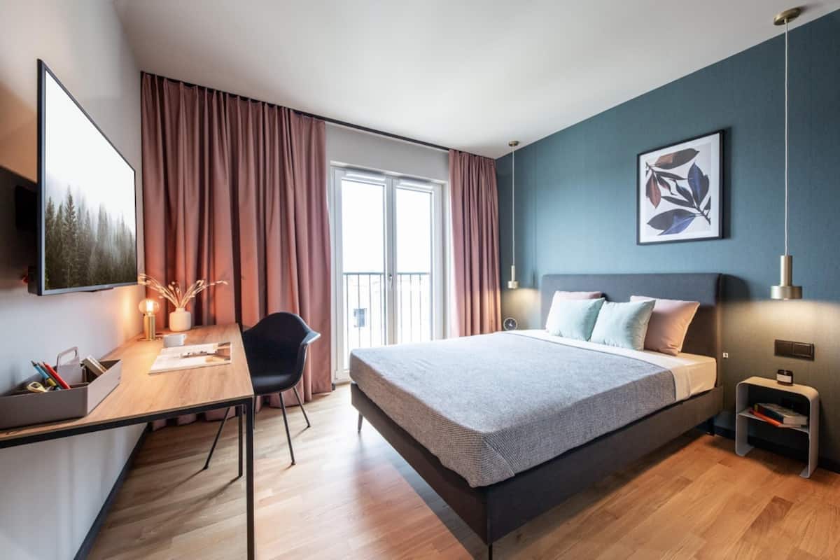 A modern bedroom with a bed, desk, chair, and artwork on the wall.