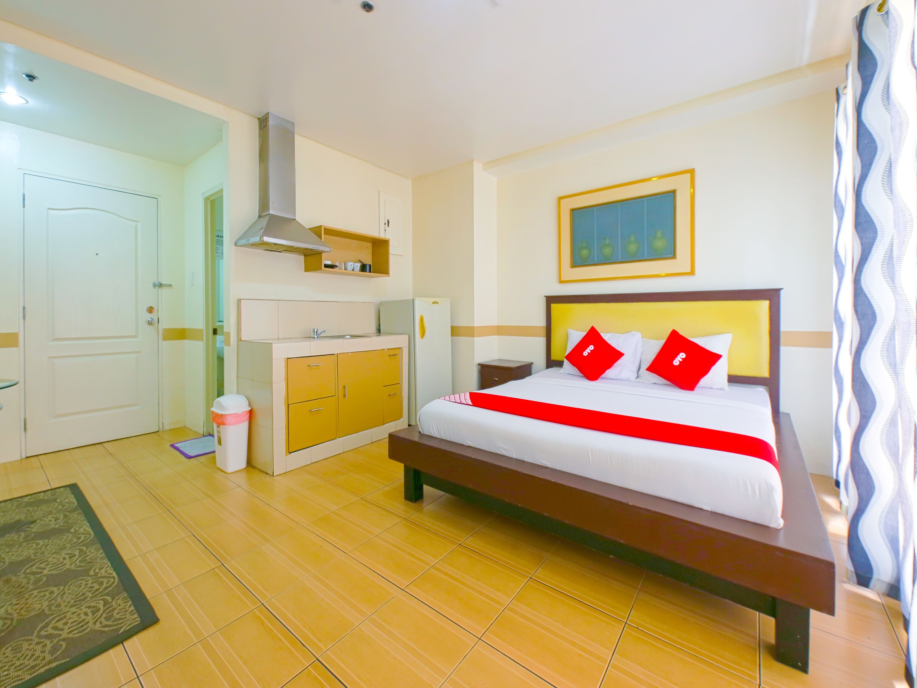 Una habitación de hotel con una cama, una kitchenette pequeña, una puerta y una ventana con cortinas.