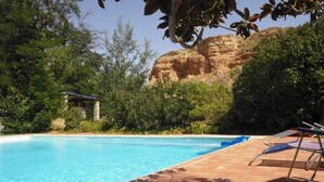 Una piscina azul cristalina con sillas de descanso, rodeada de exuberante vegetación y un acantilado rocoso.