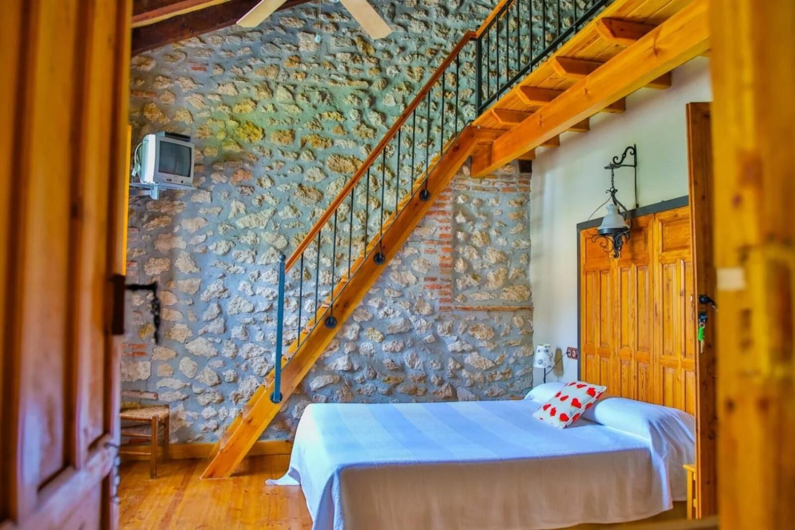 Un dormitorio con pared de piedra, escalera de madera y cama con almohada roja y blanca.