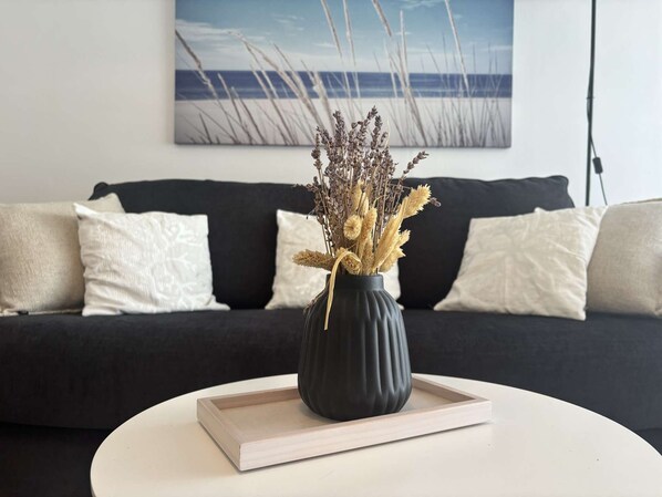 A black vase with dried plants on a white tray on a round table, with a black sofa and white pillows in the background. - Bénodet, 3 stars apartment, beach, thalassotherapy and shops on foot (BENODET)