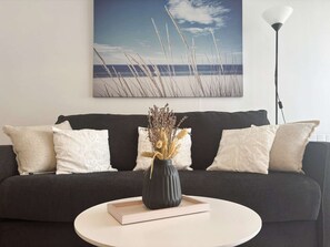 A living room with a dark sofa, white pillows, a vase with dried plants, and a book on a white coffee table. - Bénodet, 3 stars apartment, beach, thalassotherapy and shops on foot (BENODET)
