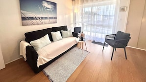 Una sala moderna con un sofá, una mesita, un sillón, un televisor y un ventanal con cortinas traslúcidas.