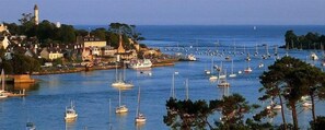 A coastal town with a harbor filled with boats, a prominent lighthouse, and buildings along the waterfront.