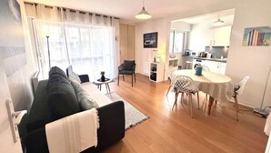 Una sala de estar moderna con un sofá, una mesa de comedor y sillas. Hay una zona de cocina con electrodomésticos y una ventana.