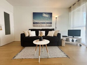 A modern living room with a black sofa, a round coffee table, and a painting of a beach scene. - Bénodet, 3 stars apartment, beach, thalassotherapy and shops on foot (BENODET)