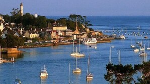 Un pueblo costero con un puerto deportivo lleno de barcos, un faro y edificios a lo largo de la costa.