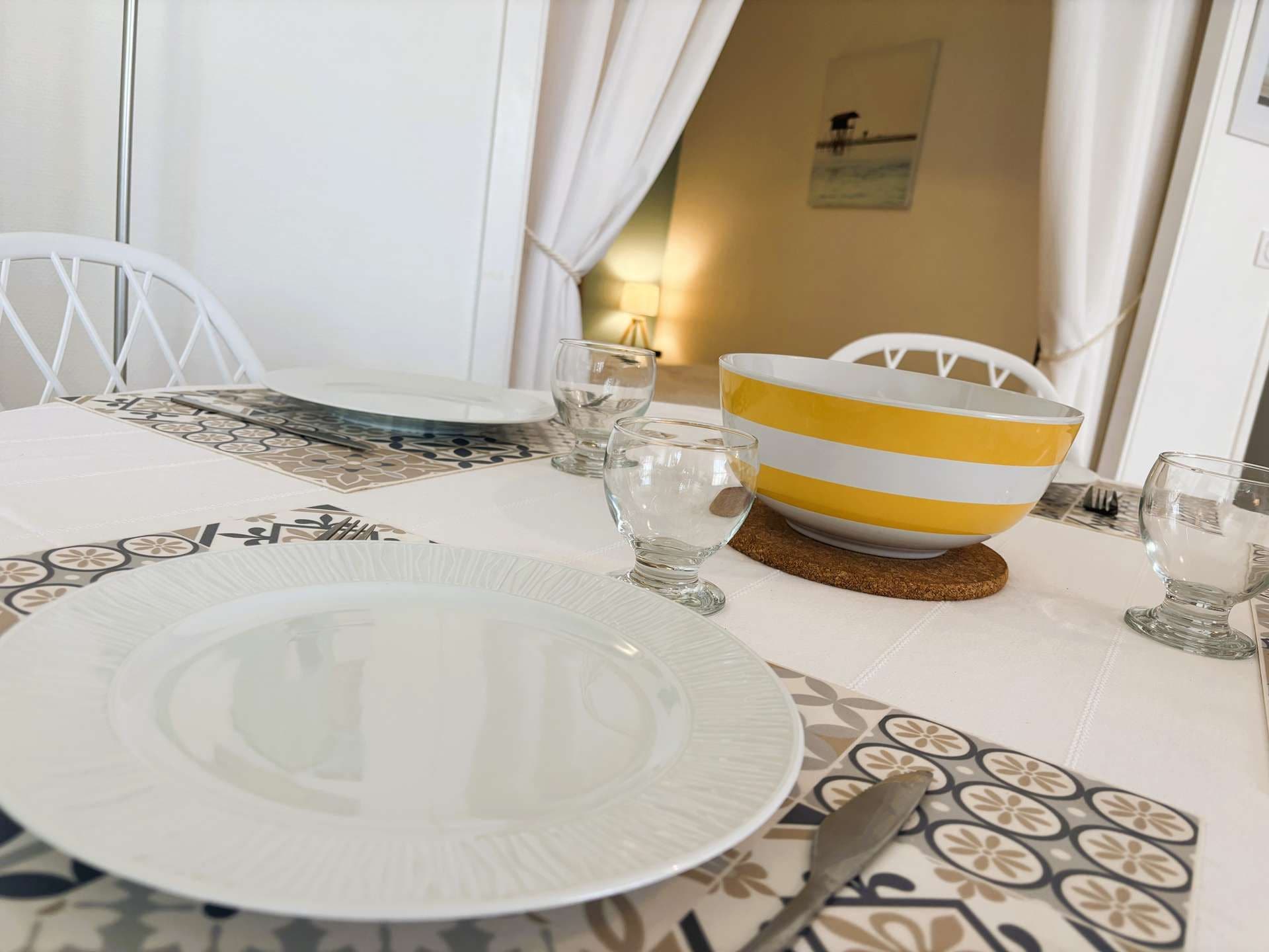 A dining table set with a white plate, a yellow and white striped bowl, and clear glasses.