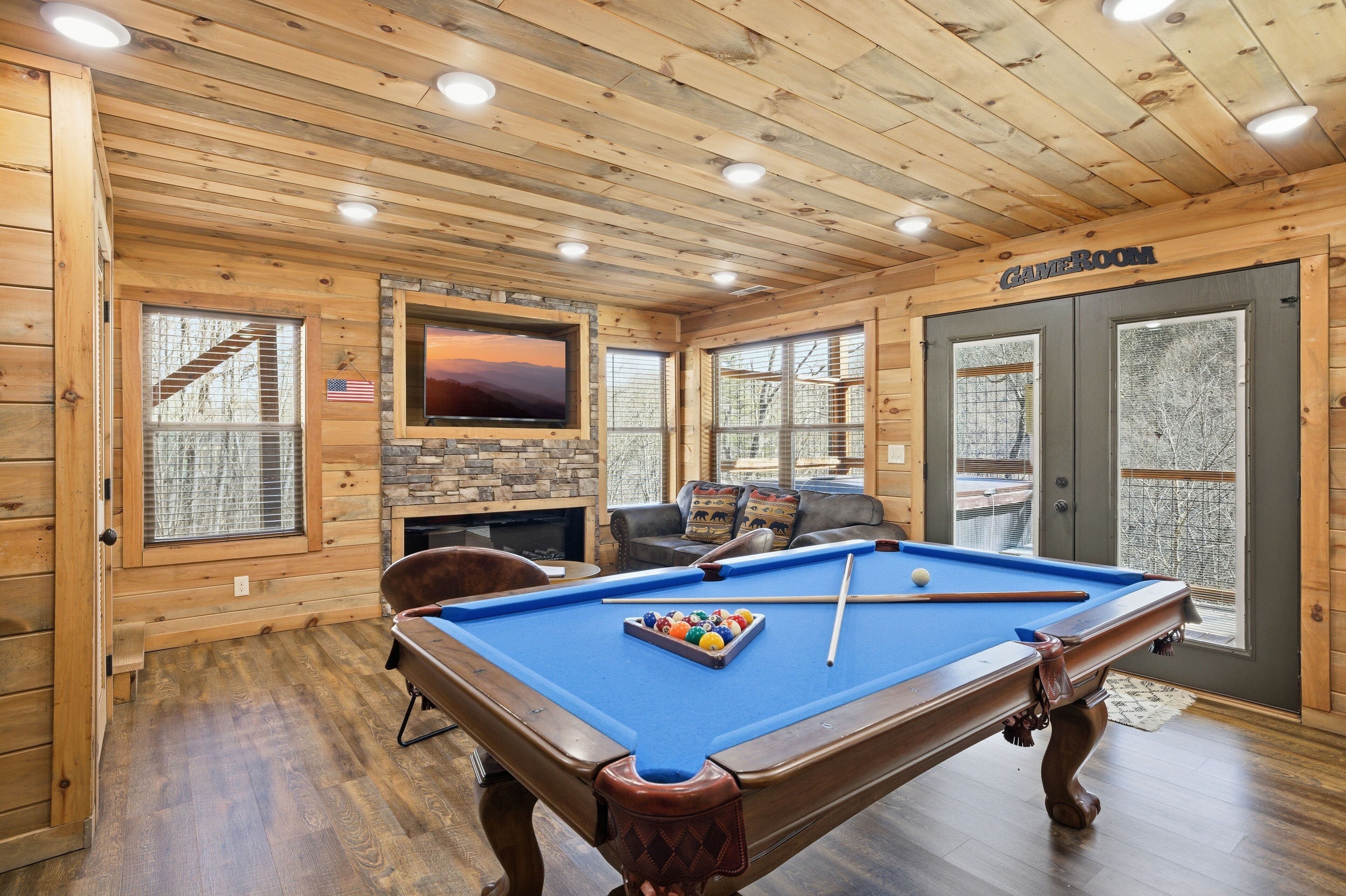 A wooden-paneled room with a pool table, a television, and a fireplace.
