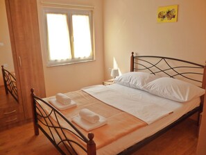 Una cama bien hecha con sábanas blancas y dos toallas enrolladas, una lámpara de noche y una ventana con cortinas.