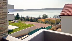 Vista desde un balcón sobre un lago con un puente distante, un área con césped y un edificio amarillo.