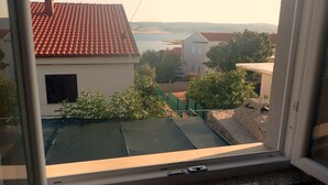 Vista desde una ventana a una zona residencial, con una casa de techo de tejas rojas, un edificio blanco con contraventana negra y una valla verde.