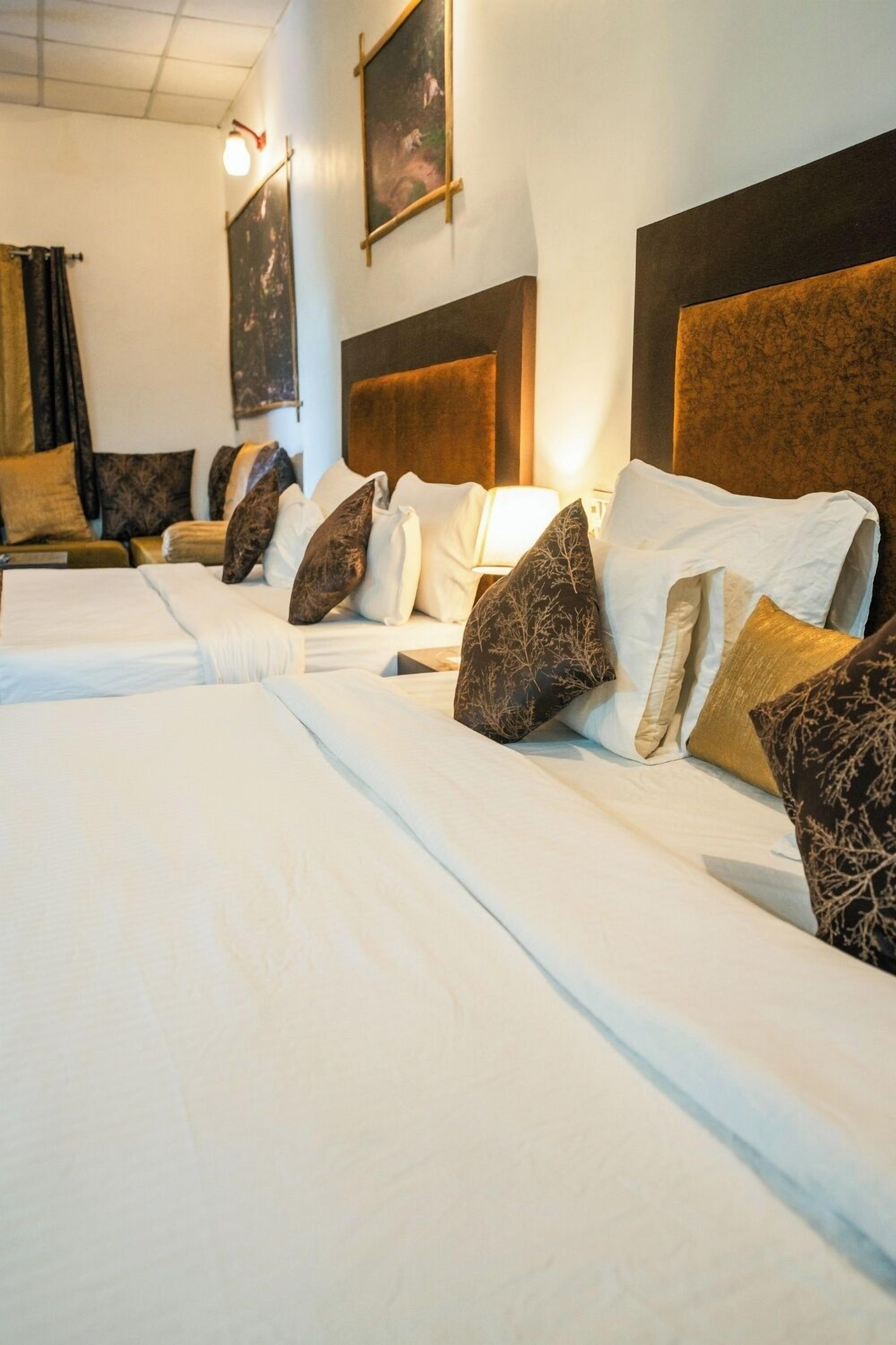 Habitación de hotel con dos camas, cada una con sábanas blancas y almohadones decorativos. La habitación tiene un cabecero de madera y un cuadro en la pared.