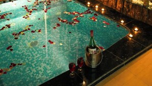 Un área de piscina con pétalos de rosa, velas y una botella de champán.