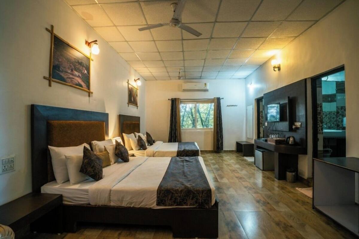 Habitación de hotel con dos camas, un escritorio, un televisor y un ventanal con cortinas.
