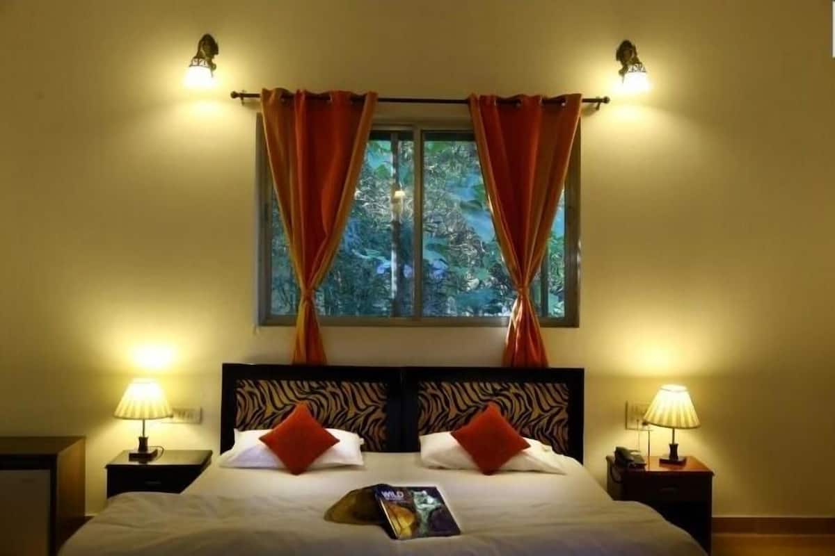 Una habitación de hotel con cama, dos mesitas de noche, ventana con cortinas y lámparas de pared.