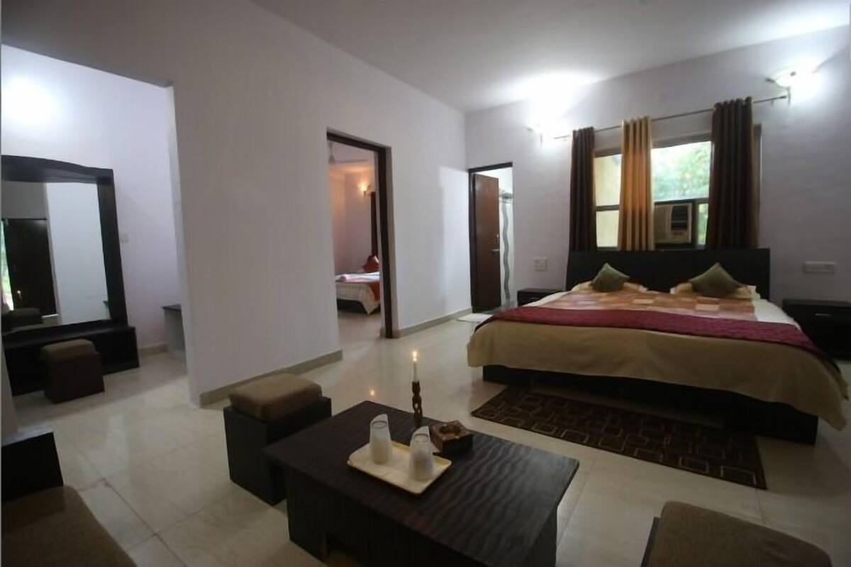 Habitación de hotel con una cama grande, zona de estar con una mesa y un espejo.