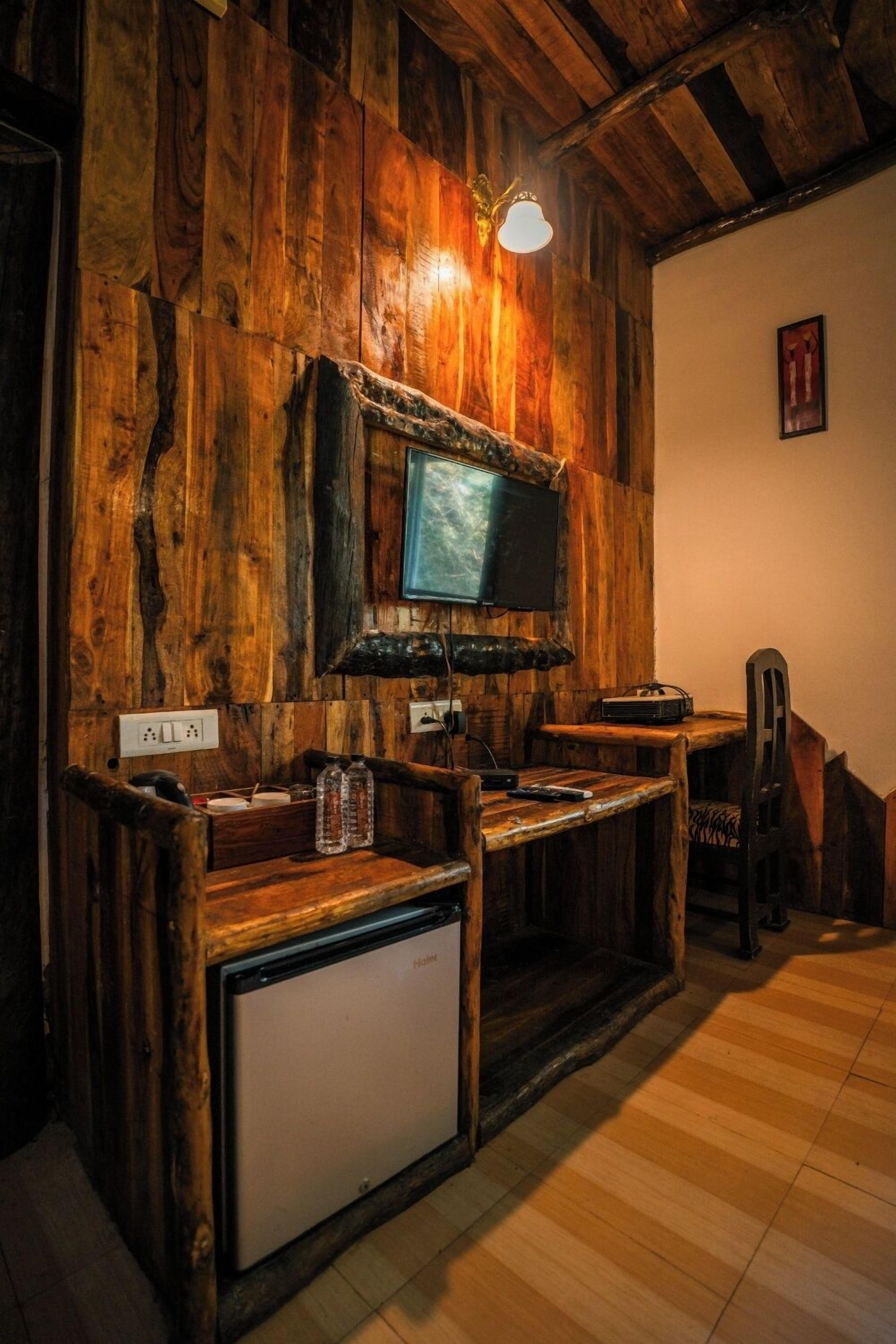 A rustic wooden bar area with a television mounted on the wall, a small refrigerator, and a wooden chair.