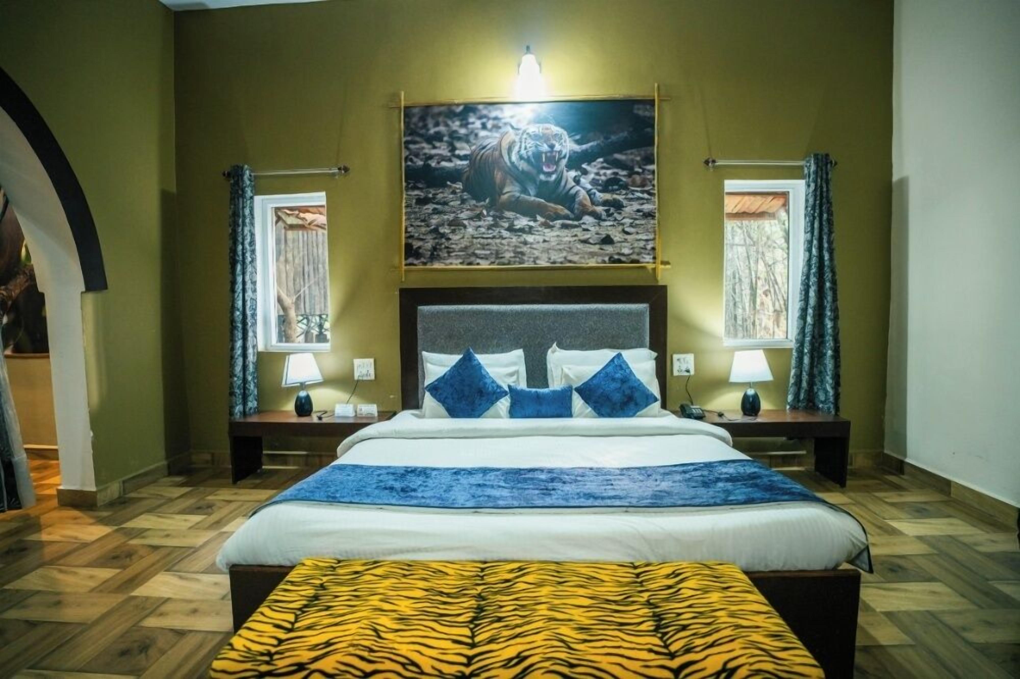 A bedroom with a large bed, two bedside tables with lamps, a headboard, a framed picture above the bed, and a window with curtains.