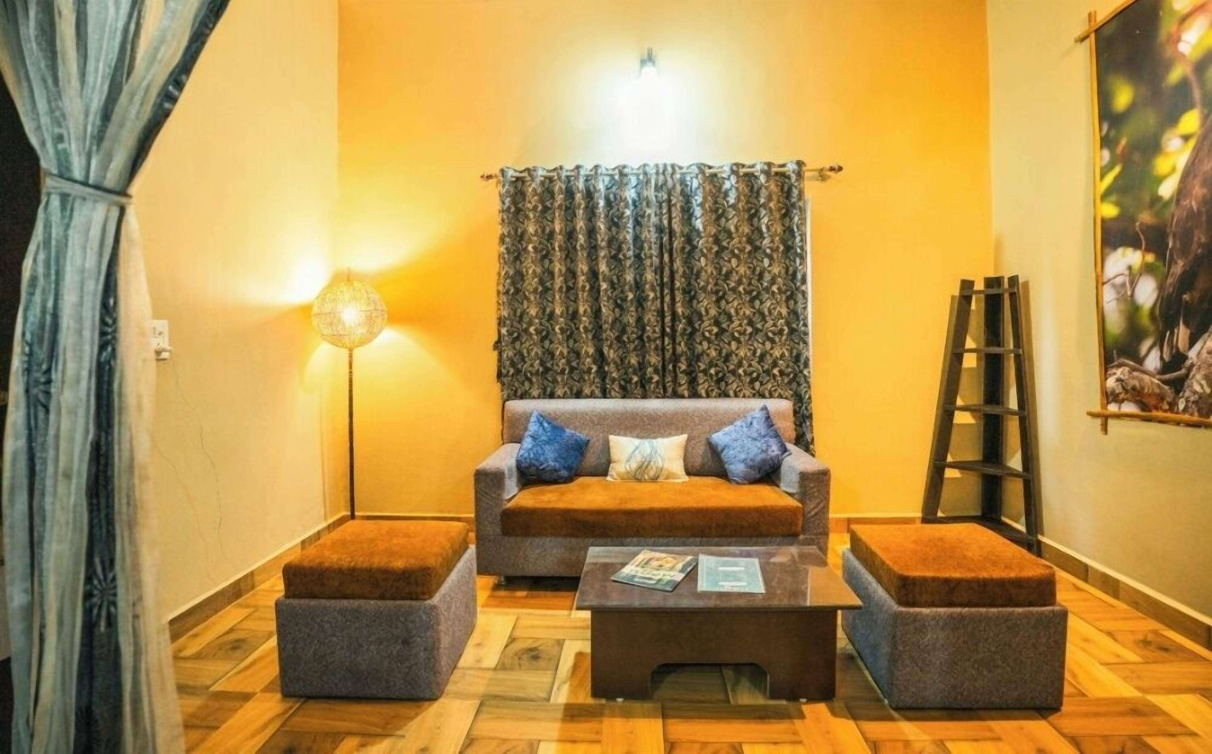 Una sala de estar acogedora con un sofá, dos otomanas, una mesita de centro y un cortinaje estampado.