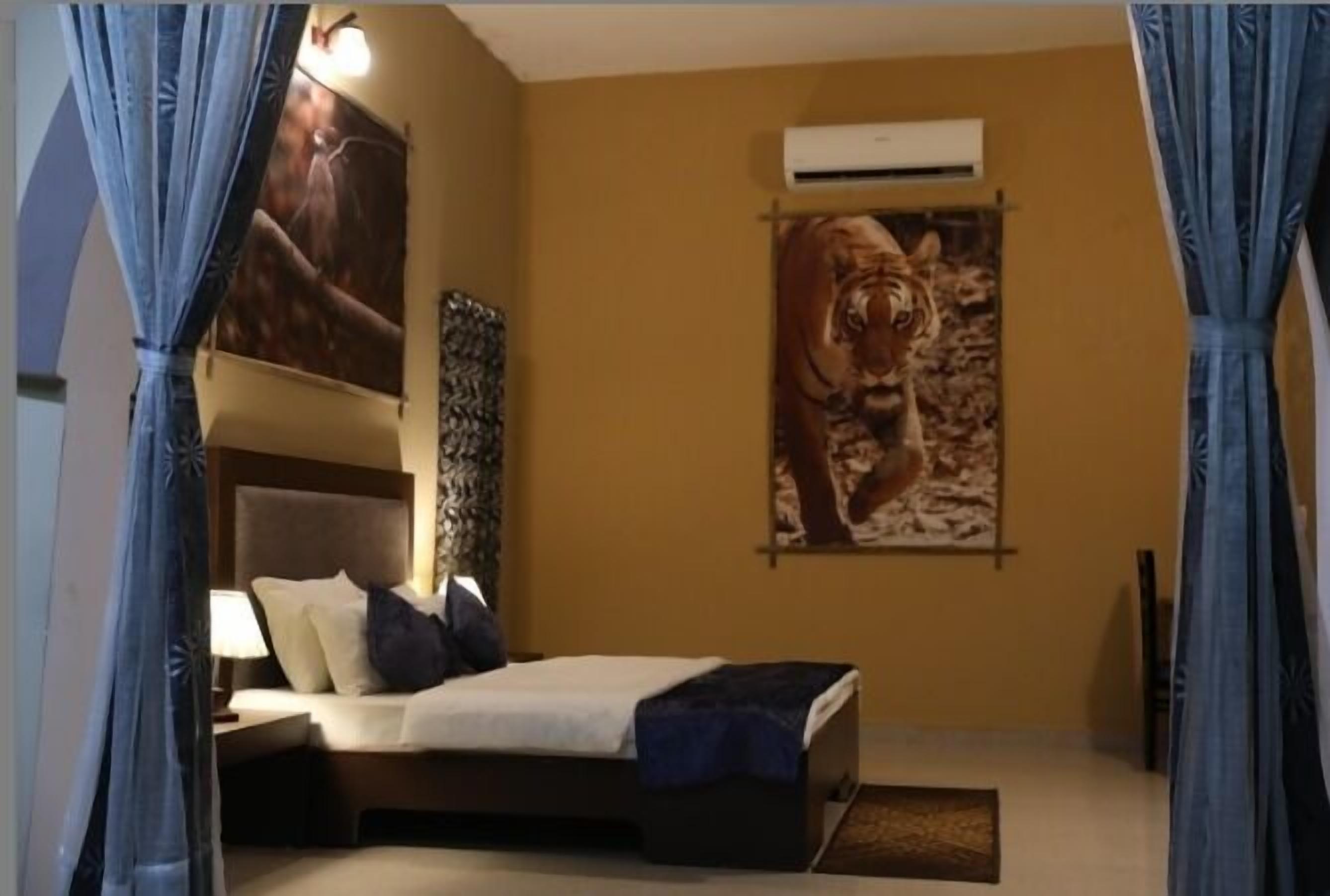 A bedroom with a bed, a nightstand, a wall-mounted air conditioner, and two large tiger posters on the wall.