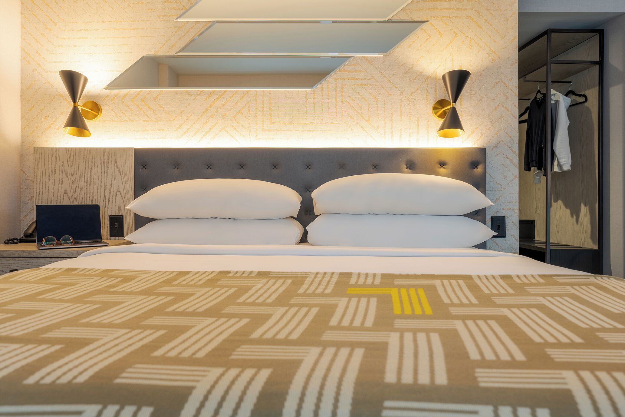 A modern hotel room with a large bed, a desk with a laptop, and a wardrobe.
