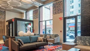 A modern lobby with a sofa, armchairs, and a coffee table. There are large windows, a red exit sign, and a patterned wall. - Pestana CR7 Times Square (New York)