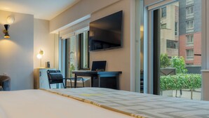 A hotel room with a bed, a desk, a chair, a TV, and a window with a view of buildings and greenery. - Pestana CR7 Times Square (New York)