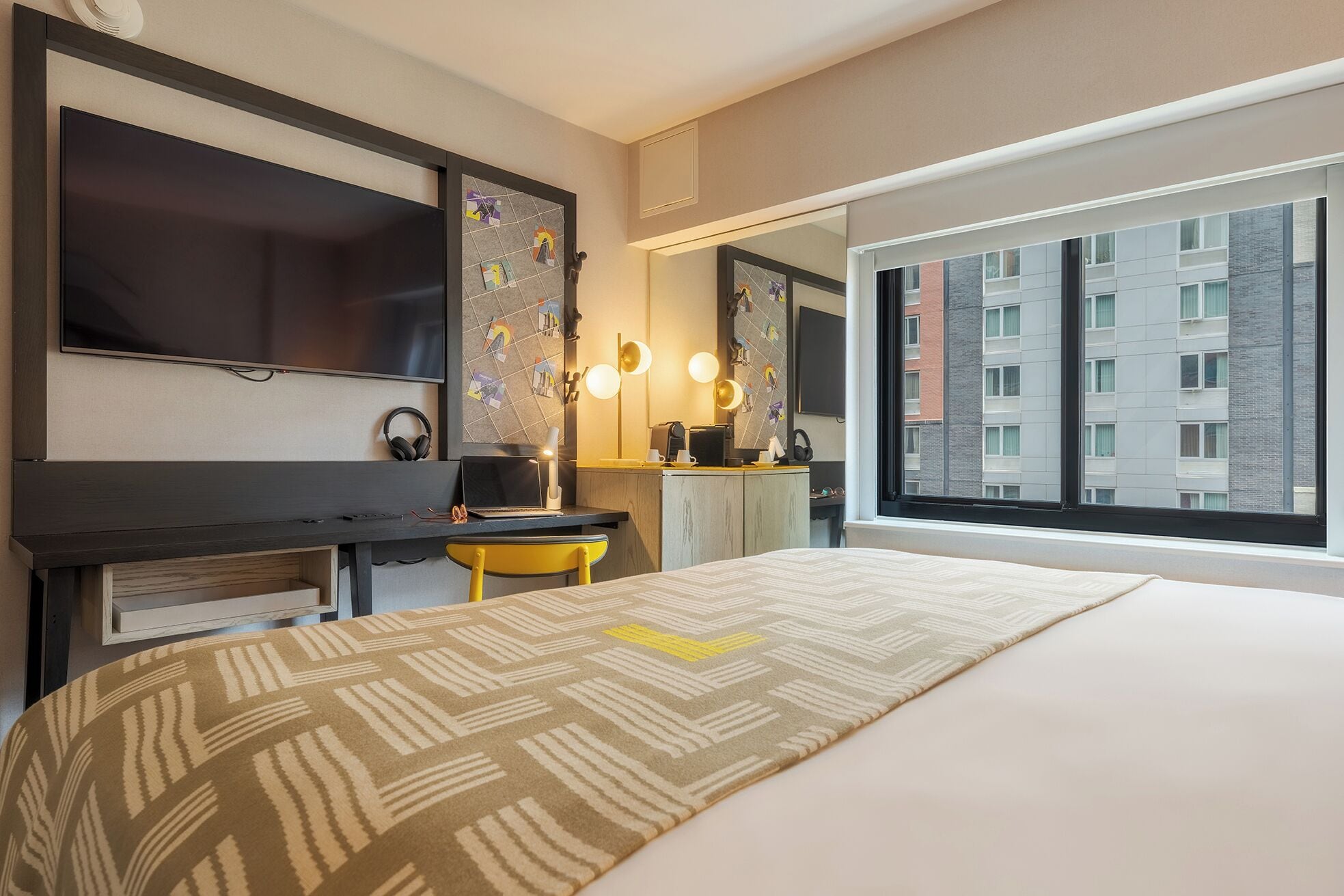 Una camera d'albergo con un letto, una scrivania con un portatile, una televisione e un'ampia finestra vista città.