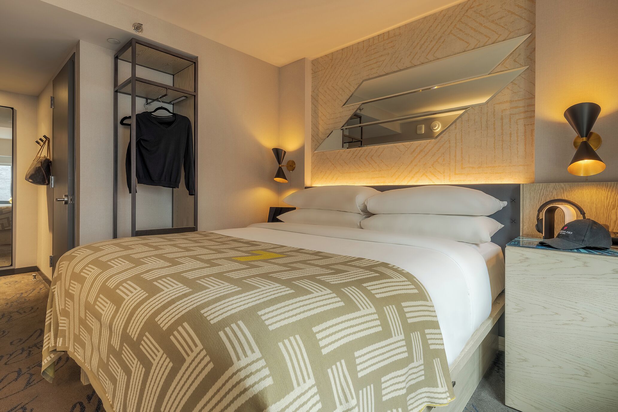 Una habitación de hotel con cama, armario, espejo y escritorio con lámpara.