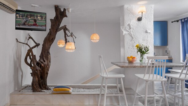 A modern kitchen with white bar stools, a wooden tree sculpture, hanging pendant lights, and a television mounted on the wall. - Villa Cissa Apartments by Irundo (Rovinj)