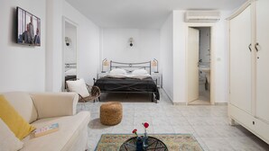 A modern bedroom with a bed, a sofa, a wicker chair, a small table with a vase, and an open bathroom door. - Villa Cissa Apartments by Irundo (Rovinj)