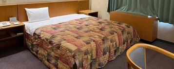 Una habitación de hotel con cama, mesita de noche con teléfono, silla y ventana con cortinas.