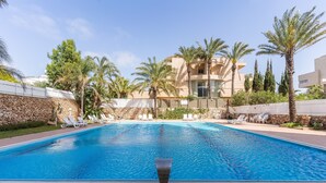 A swimming pool with lounge chairs, palm trees, and a stone wall. - Top Tier Apartment with Swimming Pool (Herzliya)