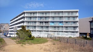 Un hôtel à plusieurs étages doté de balcons, avec une plage de sable devant et un ciel bleu dégagé.