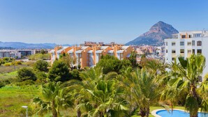 Ein Resort mit mehreren Gebäuden, einem Berg im Hintergrund und einem Poolbereich mit Palmen.