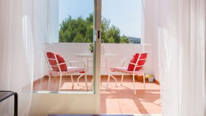Ein Balkon mit zwei weißen Stühlen und einem kleinen Tisch, mit Blick auf eine grüne Landschaft.