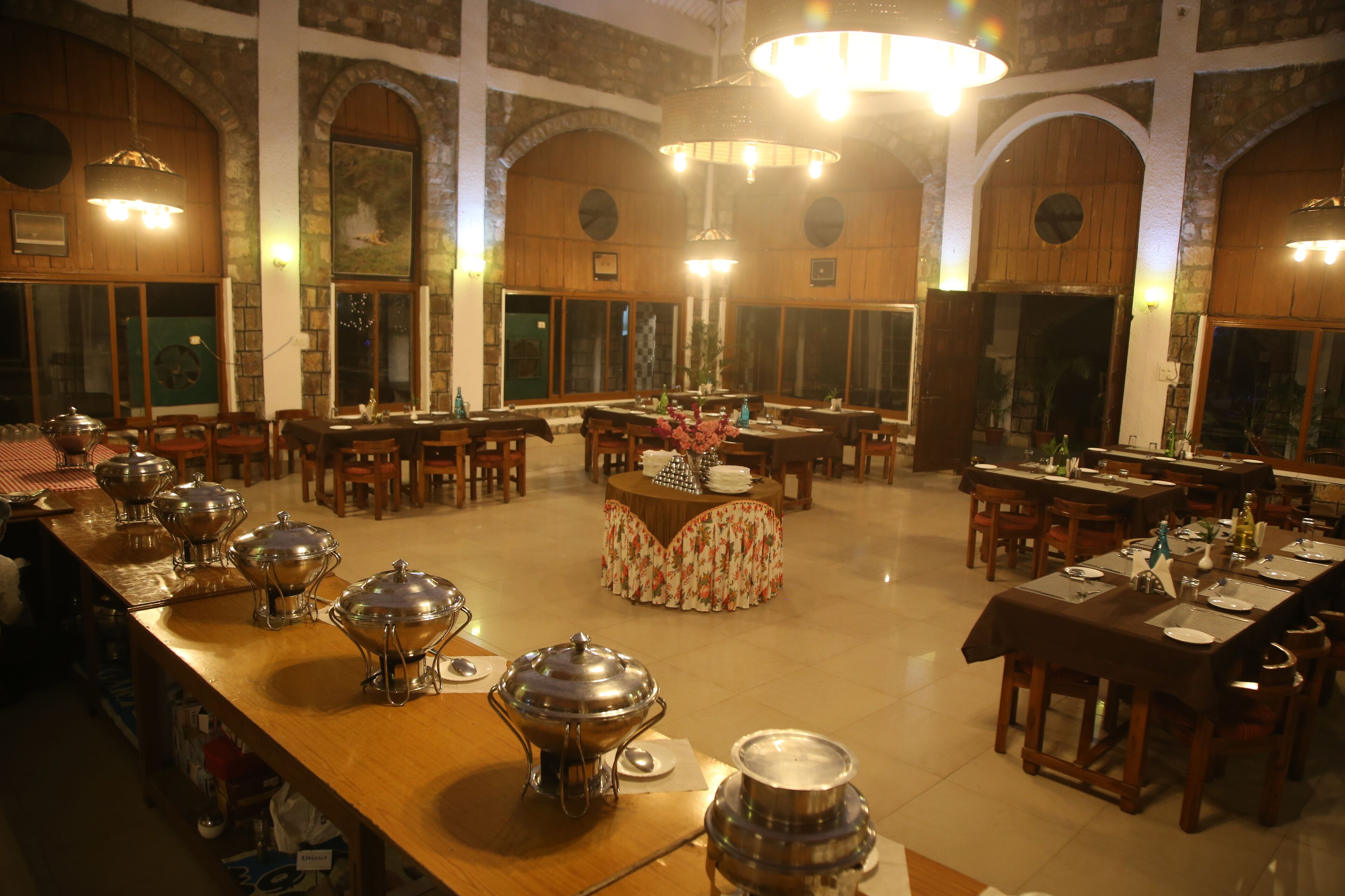 A spacious dining area with multiple tables and chairs, a buffet setup with food containers, and a chandelier.