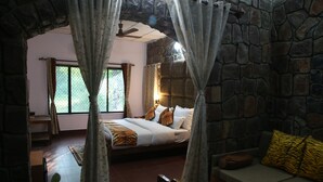 A bedroom with a stone wall, a bed with tiger-patterned bedding, a wooden bench, and a window with curtains.