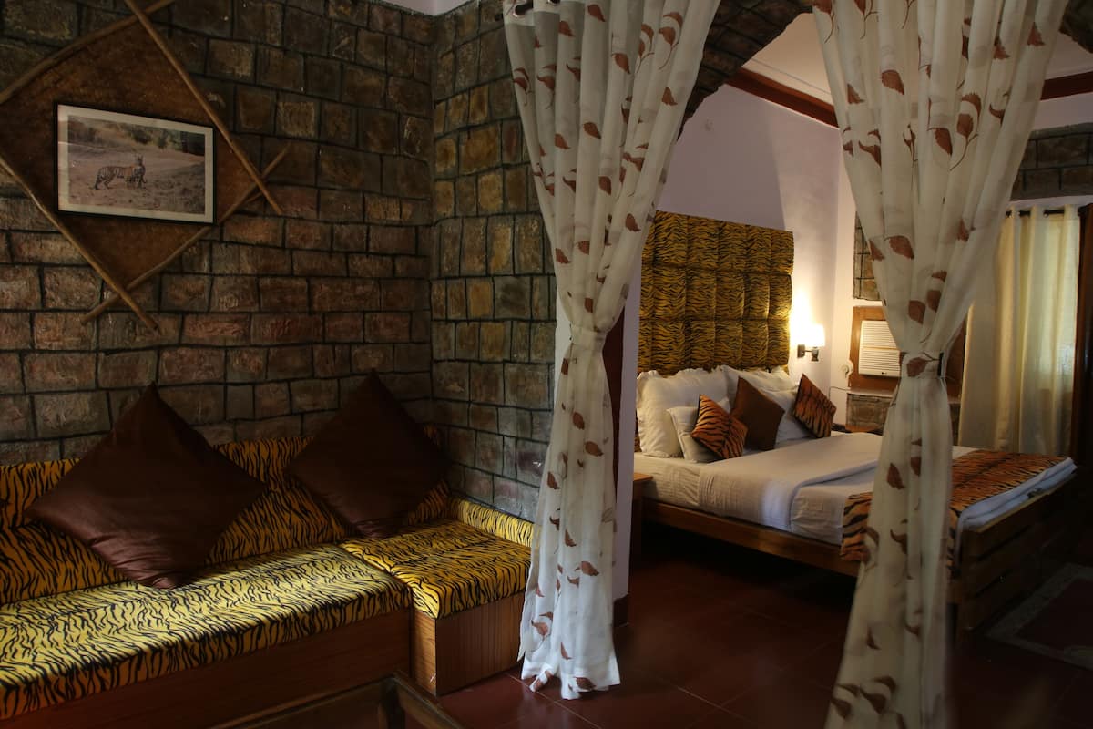 A room with a stone wall, a bed with patterned bedding, a sofa with tiger print cushions, and a picture on the wall.