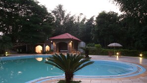 A swimming pool with a tiled deck, a palm tree, and a small pavilion with lights.