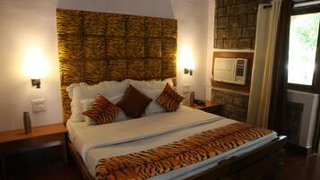 Cama com cabeceira estampada de tigre, roupa de cama branca e manta com padrão de tigre. Há duas mesas de cabeceira com luminárias e um ar condicionado fixado na parede.