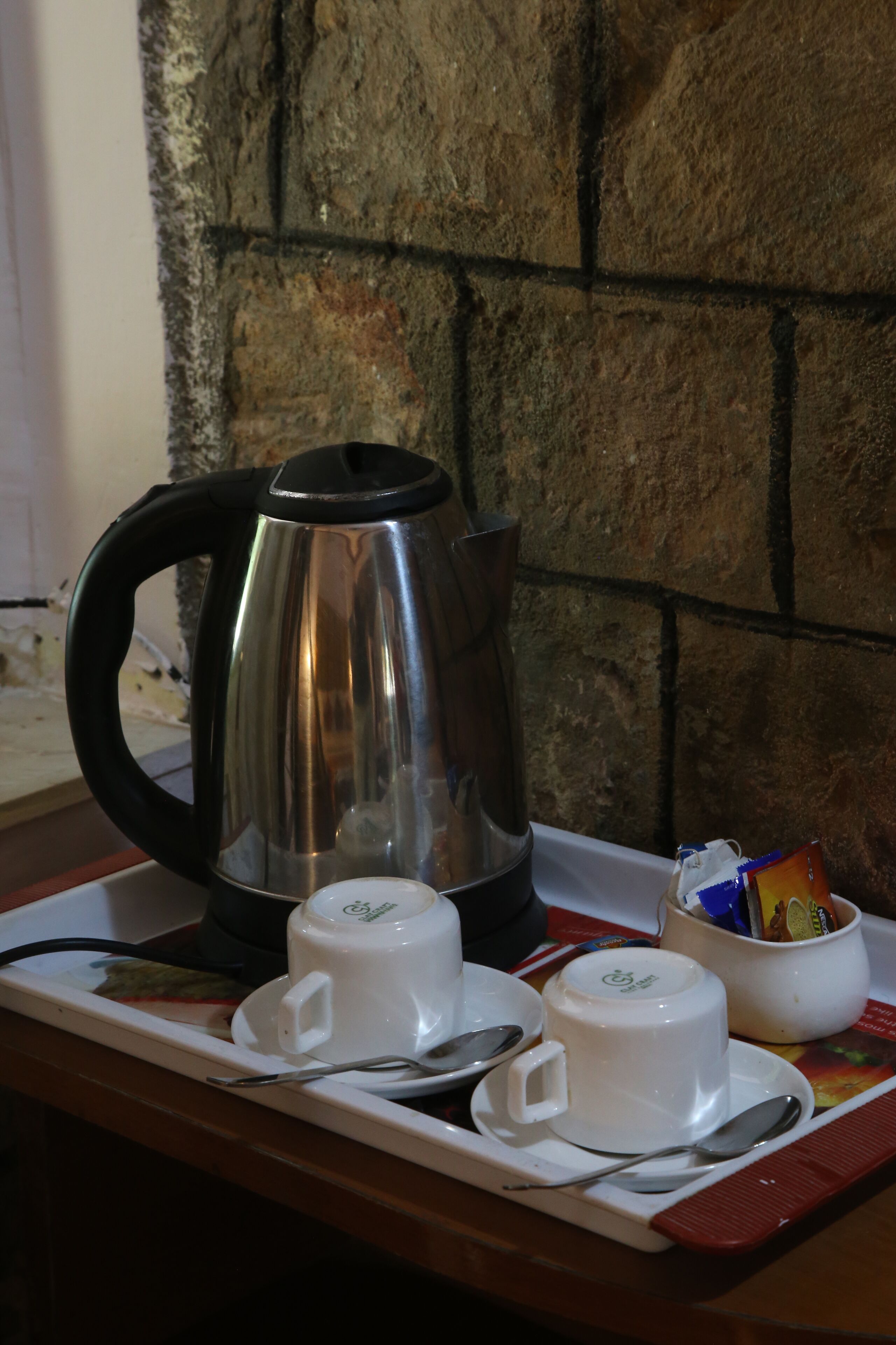 A tray with a stainless steel coffee pot, two white cups with lids, a white cup with a lid, and a small bowl with snacks.