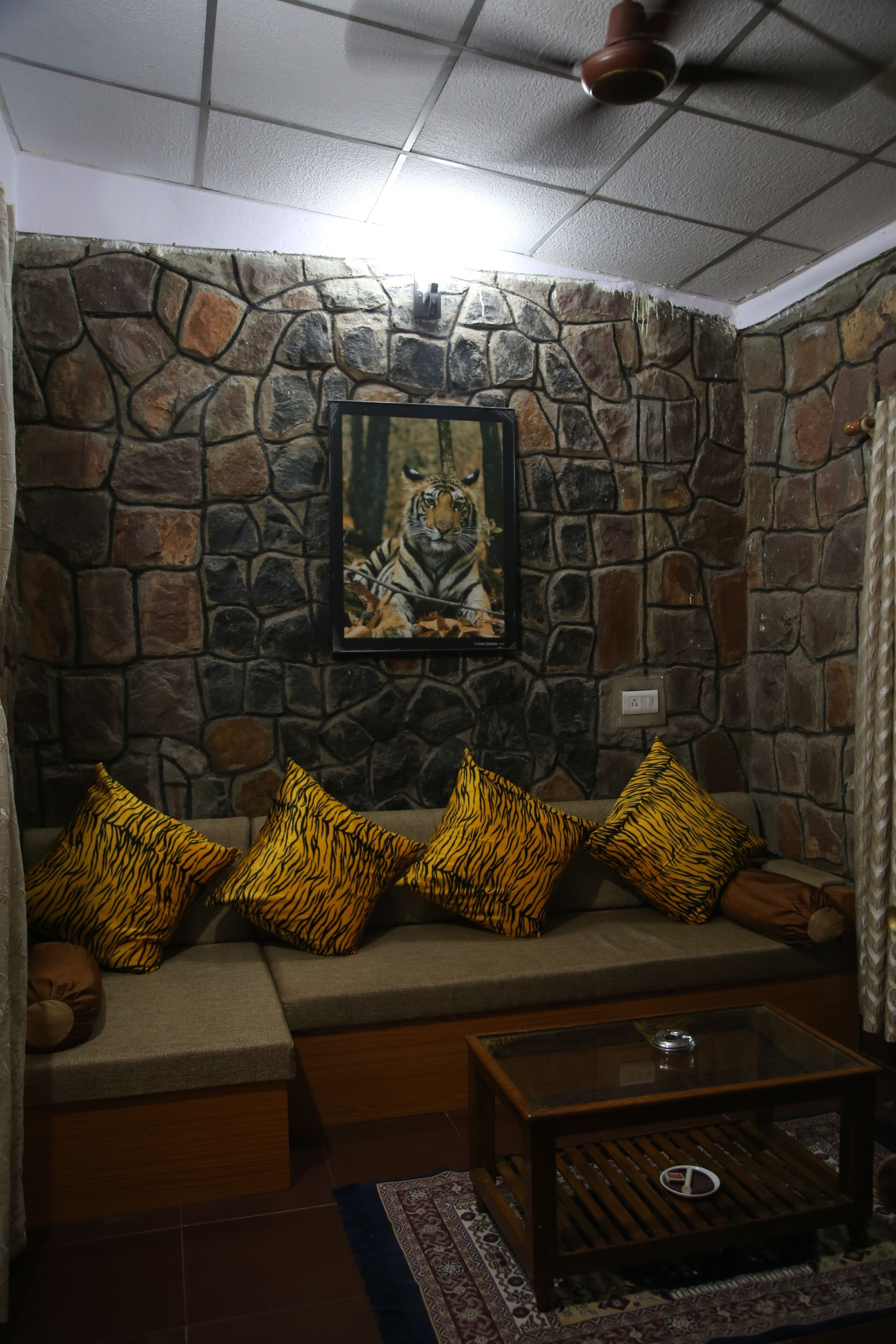 A stone wall with a framed tiger painting, a sofa with tiger-patterned cushions, and a wooden coffee table.