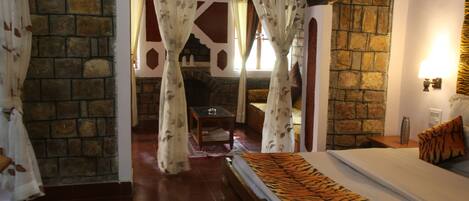 A room with a stone wall, a bed with a tiger print bedspread, and a small table with a lamp.