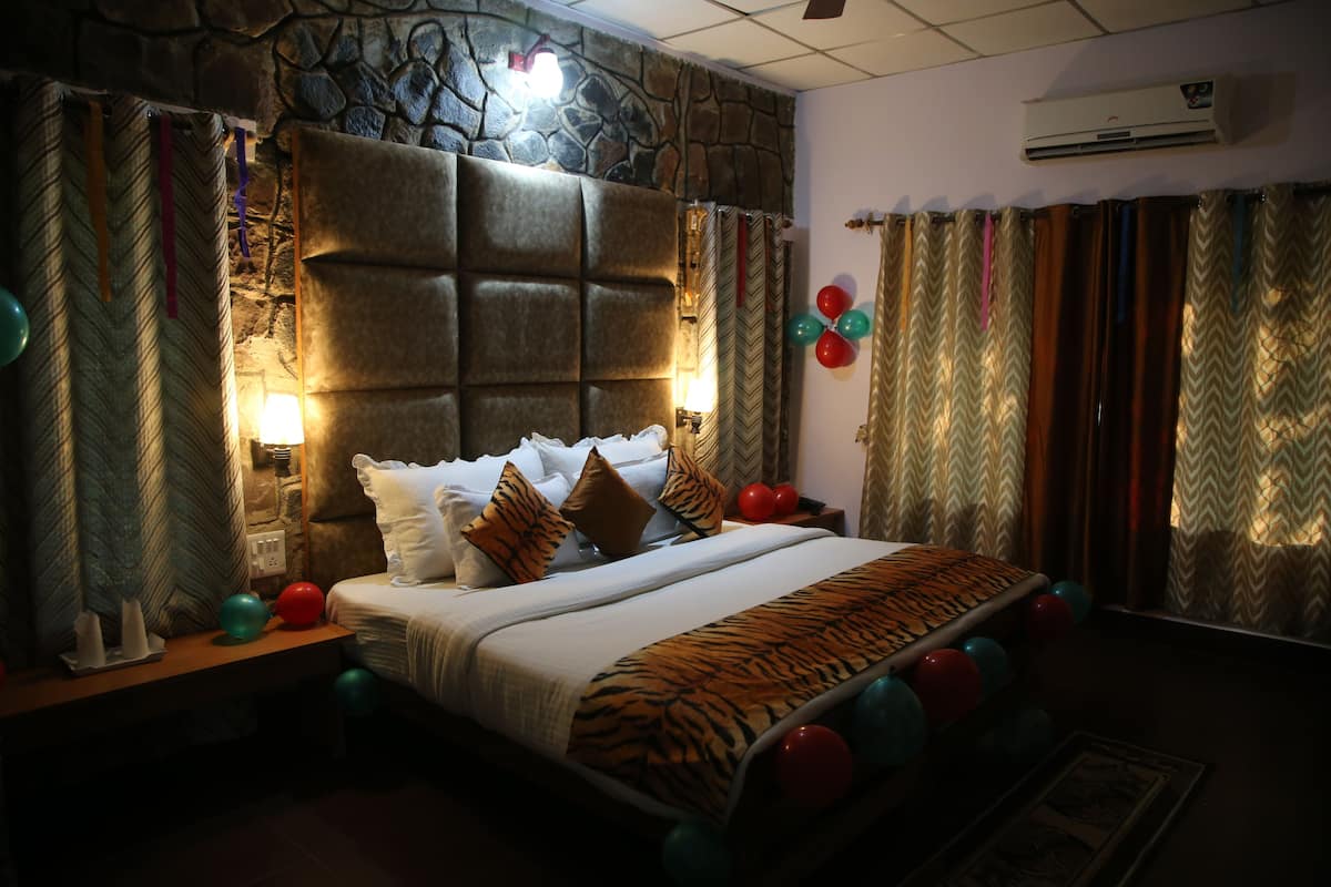 A bedroom with a stone headboard, a bed with white bedding and a tiger print throw, a nightstand with a lamp, and a wall-mounted air conditioner.