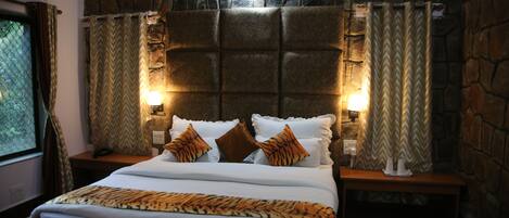 A bedroom with a stone wall, a bed with white bedding and patterned pillows, and two bedside lamps.
