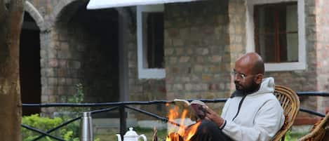 Ein Mann sitzt vor einem Feuer in einem Korbsessel, ein Tisch steht davor.